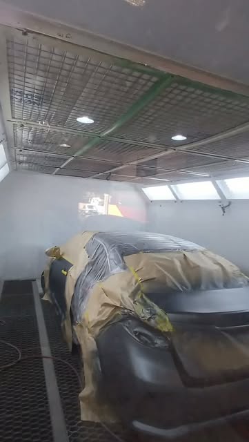Interior de la cabina de pintura del taller con luces en el techo y un auto cubierto